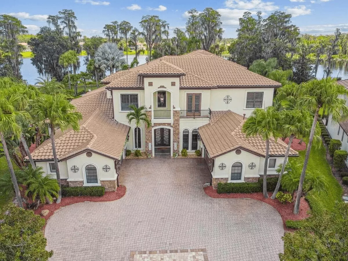 Aerial front view of a luxurious two story Mediterranean wooded lakefront home with an expansive motor court