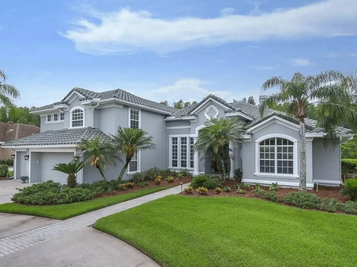 Front view of an amazing gray coastal style home with tropical landscaping and 3 car garage
