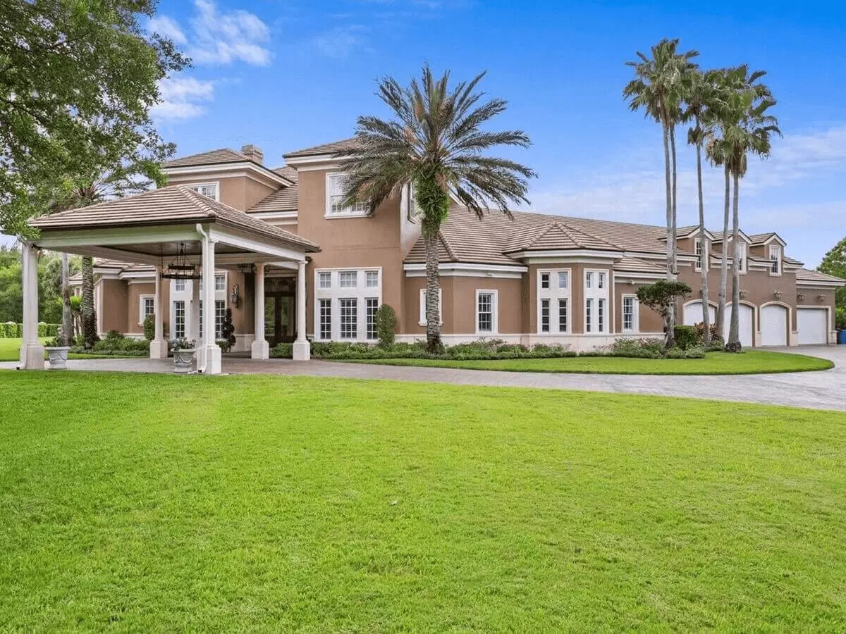 Front view of a luxury estate home with covered drive through entry and towering palm trees