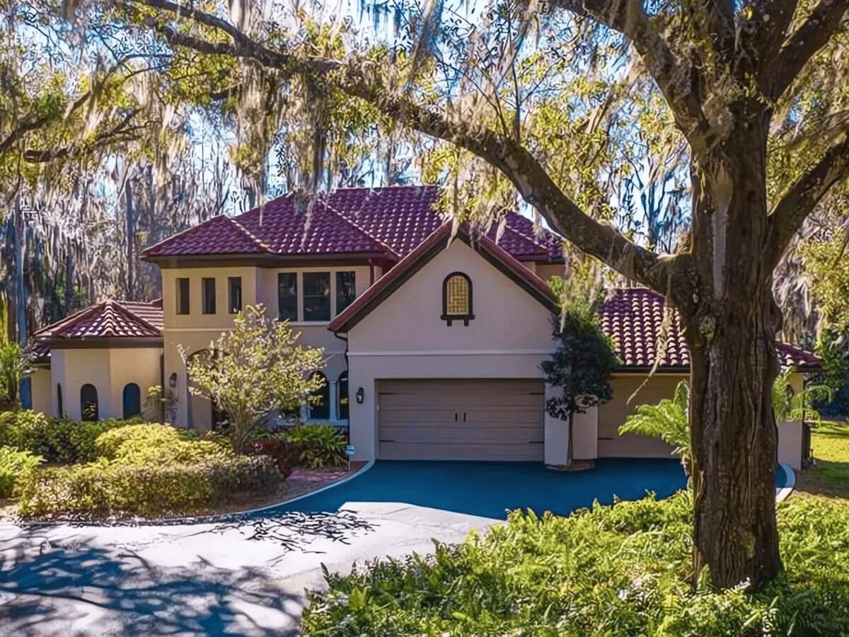 Front view of a beautiful two story wooded estate with red tile roof and mature Spanish moss trees