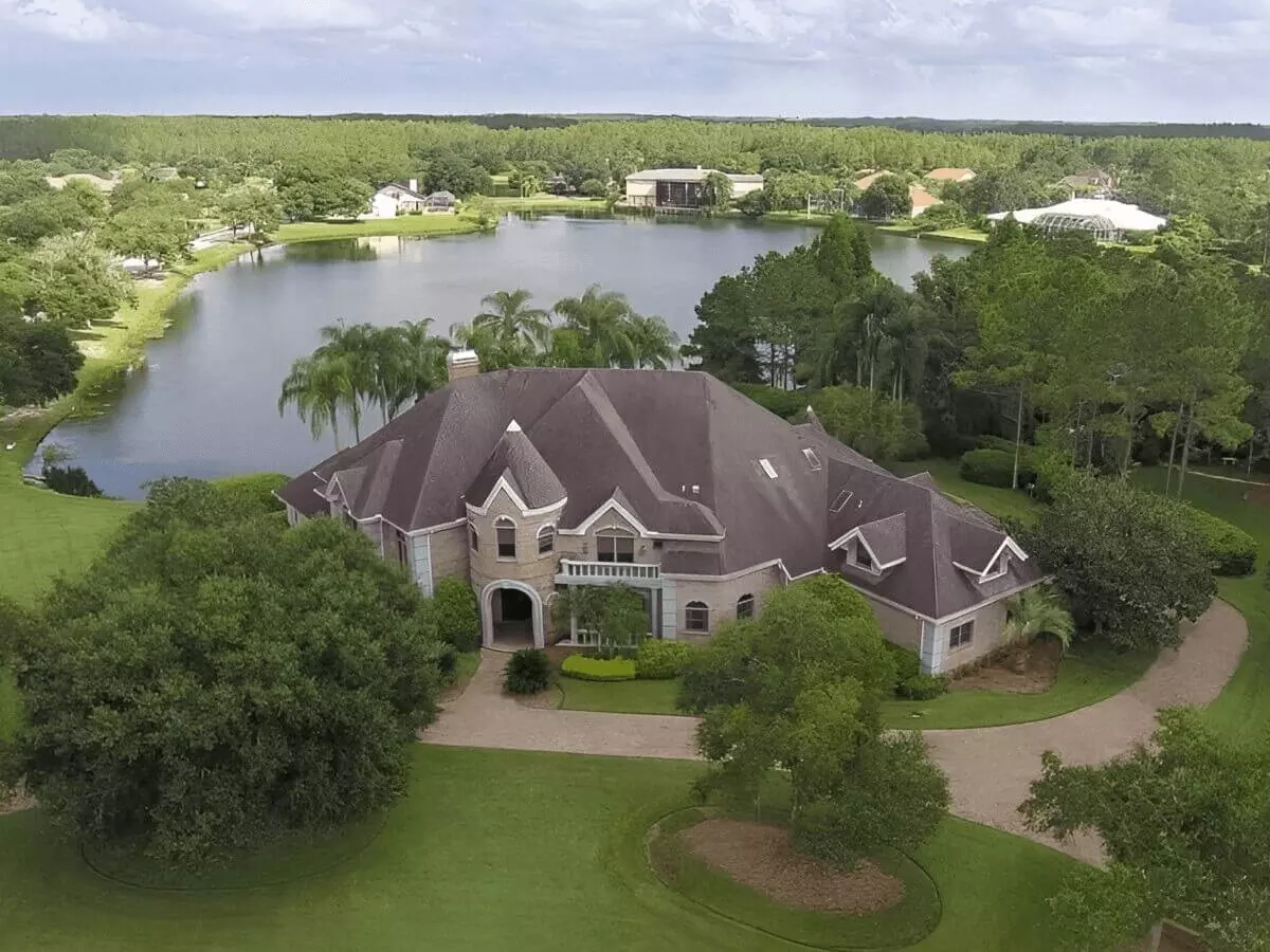 Ariel view of an expansive 2 story waterfront Estate with wraparound paver motor court surrounded by mature trees
