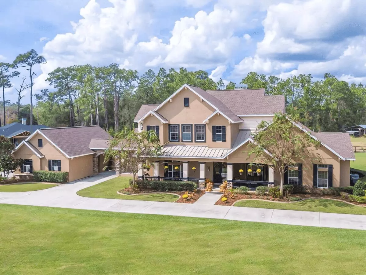 Front view of a country estate two story home on acreage with wraparound porch