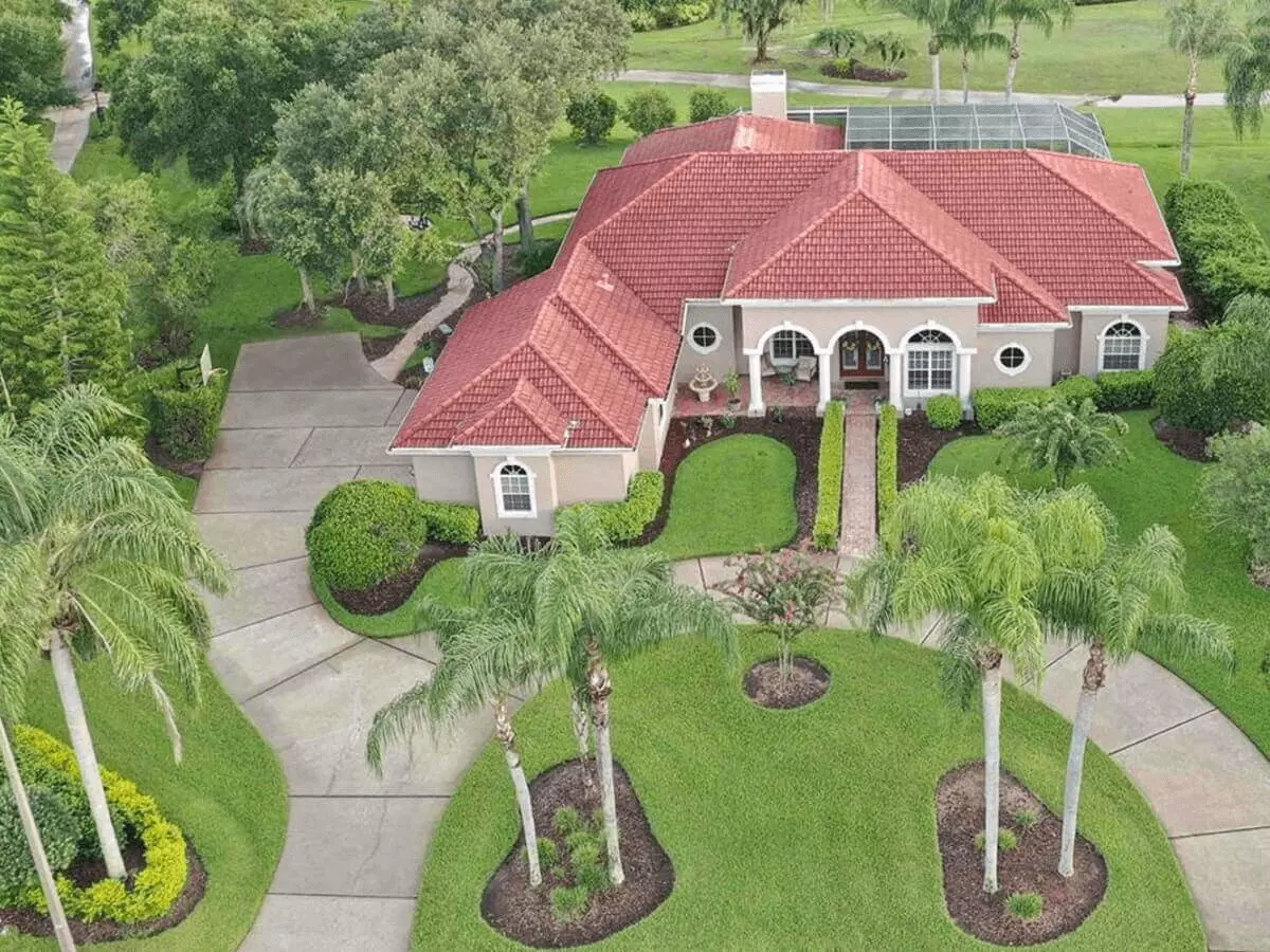 Aerial view of a Mediterranean luxury estate with palm lined motor court, screen pool on a golf course